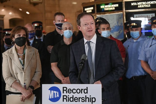 Richard Davey in a suit stands at a lectern that has a sign that says "Ridership record" at Grand CEntral Terminal